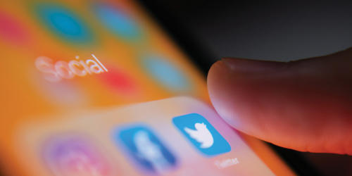 close up photo of a mobile phone screen with social media icons and a thumb about to press one